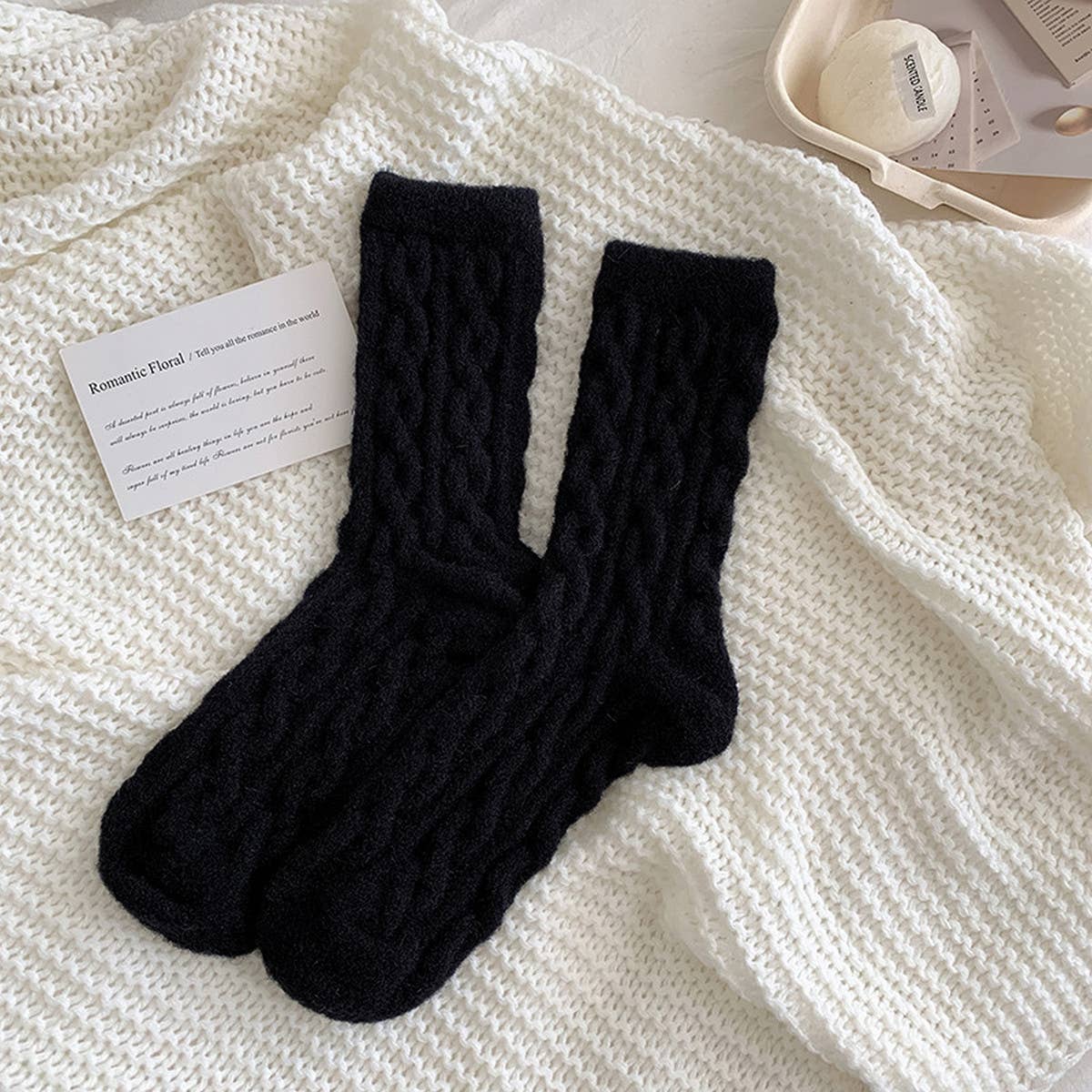 Pair of black knitted socks on a white textured surface with a card beside them.