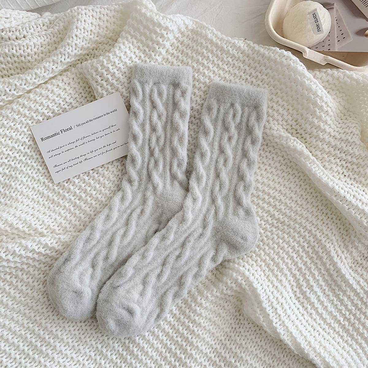 Pair of gray cable knit socks on a textured white surface with a card.