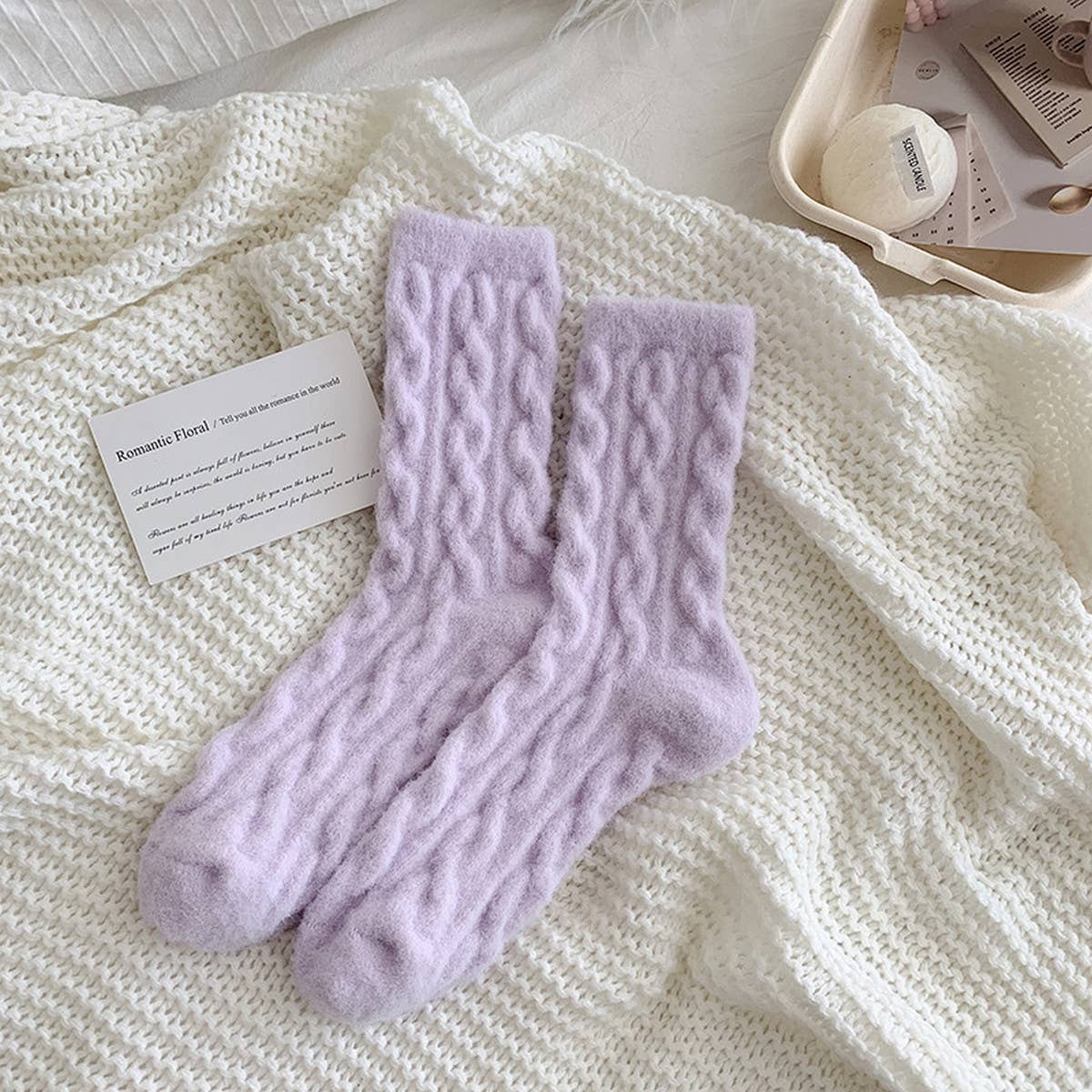 Pair of purple cable knit socks on a white textured surface with a card beside them.