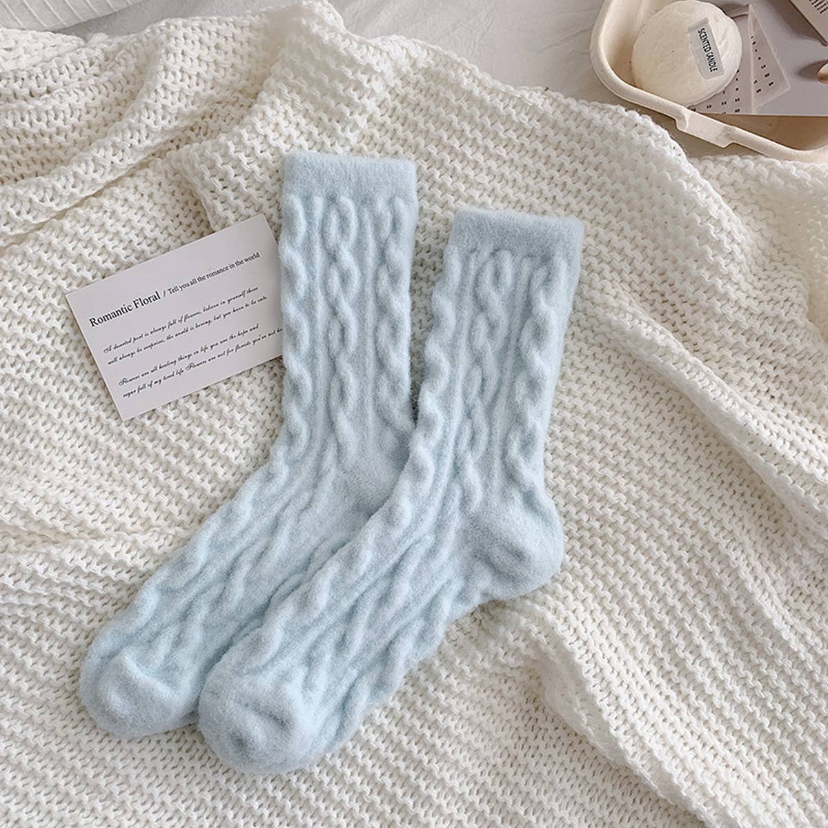 Pair of light blue cable knit socks on a textured white surface with a card.