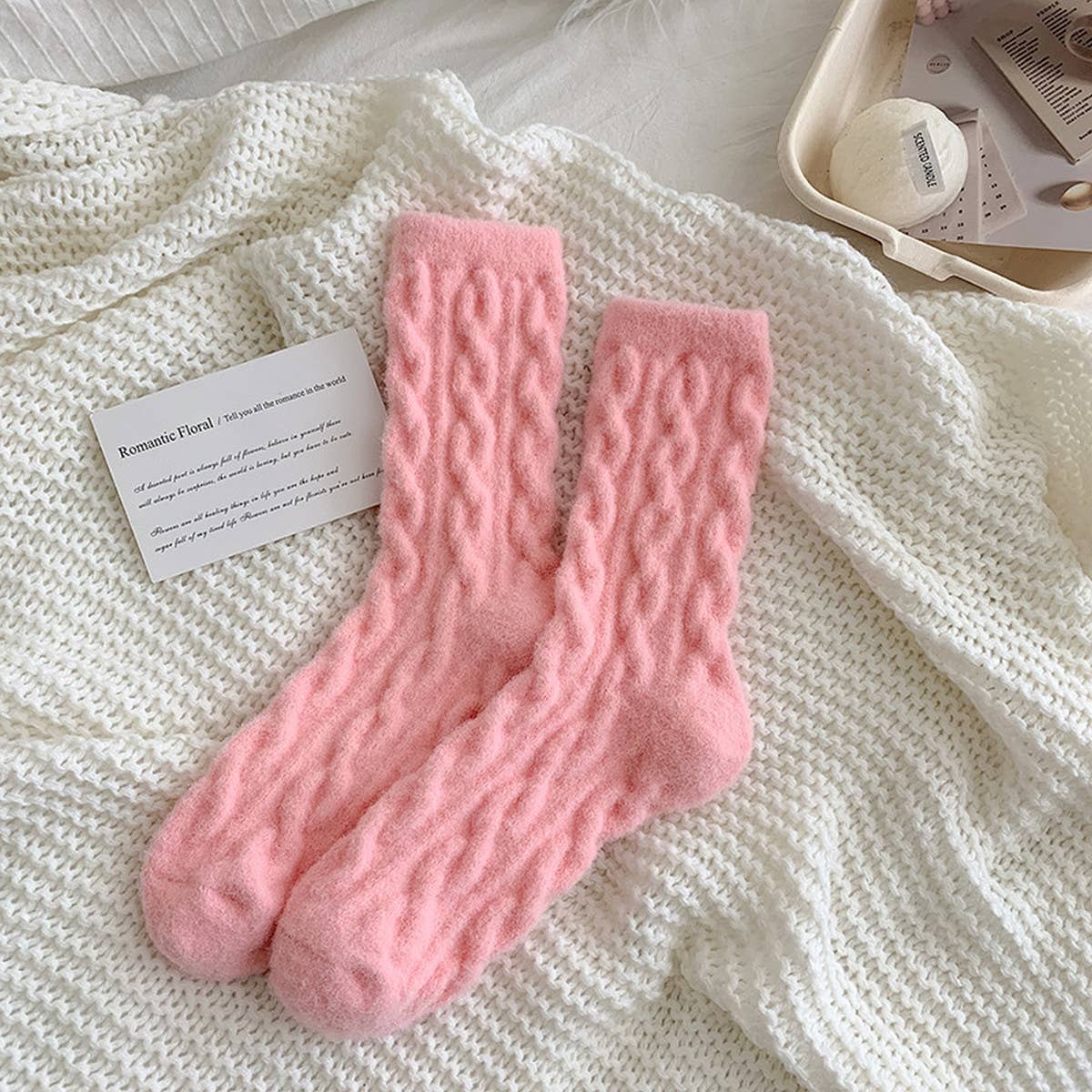Pair of pink knitted socks on a white textured surface with a card beside them.