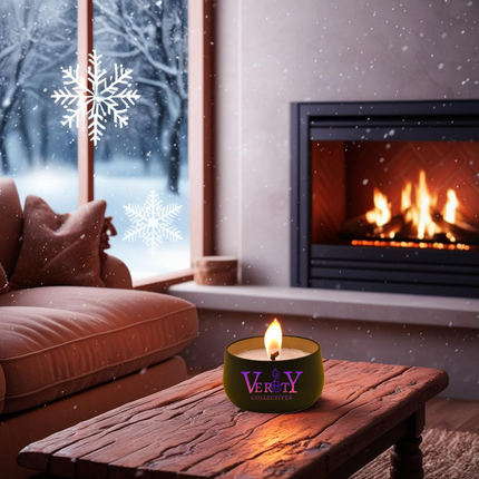 Verity Collectives lit black luxury candle sitting on wood coffee table with a lit fireplace, couch, and snow outside of the window