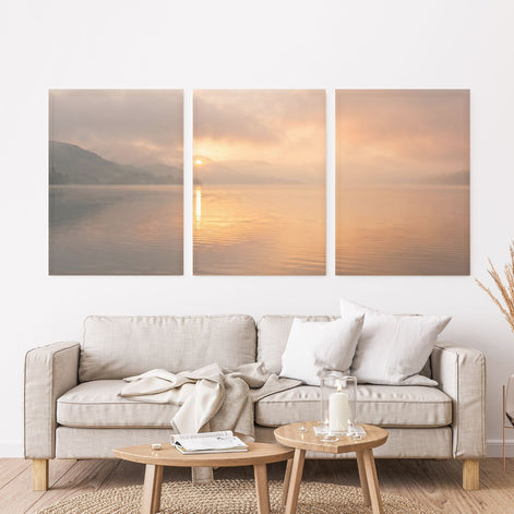 Three-panel golden sunrise lake canvas set with misty hills, a low sun, and warm peach reflections on the water