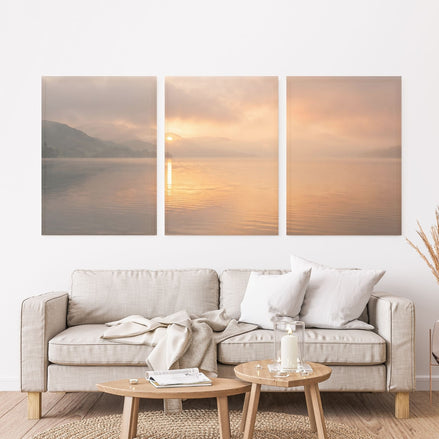 Three-panel golden sunrise lake canvas set with misty hills, a low sun, and warm peach reflections on the water