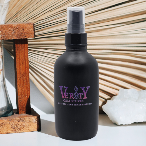 Verity Collectives room and linen spray on a white table with a wicker fan and a piece of sea salt in the background