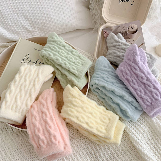 Set of pastel-colored textured towels on a white surface with a book and cat toy in the background.