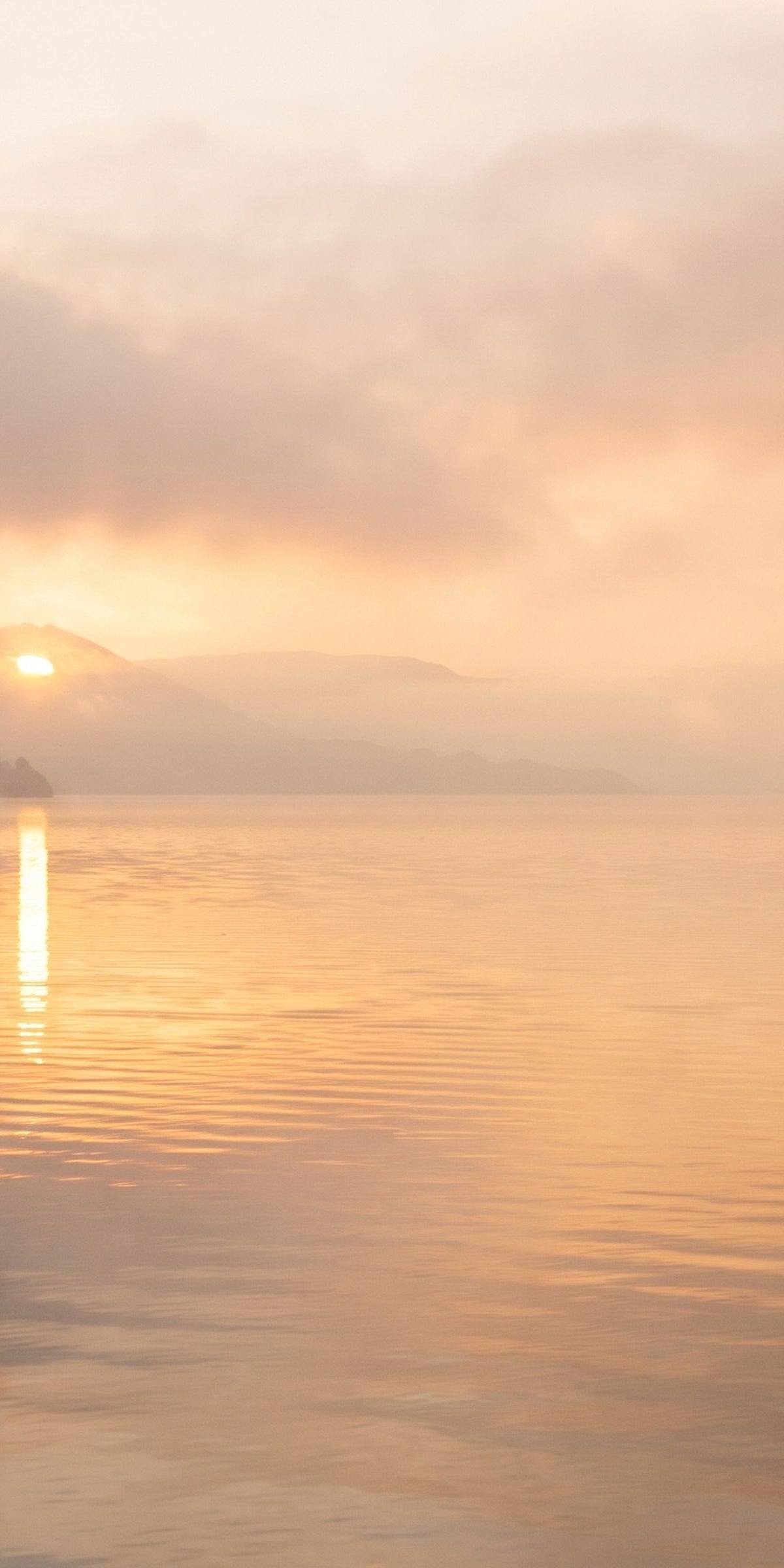 A serene landscape print of a calm lake at sunrise, featuring soft golden-orange clouds, a low sun reflecting on the water, and distant misty mountains.